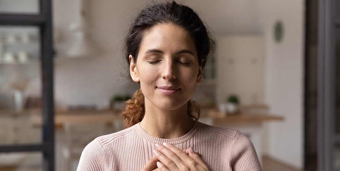 A woman takes a deep breath while holding her hands against her chest