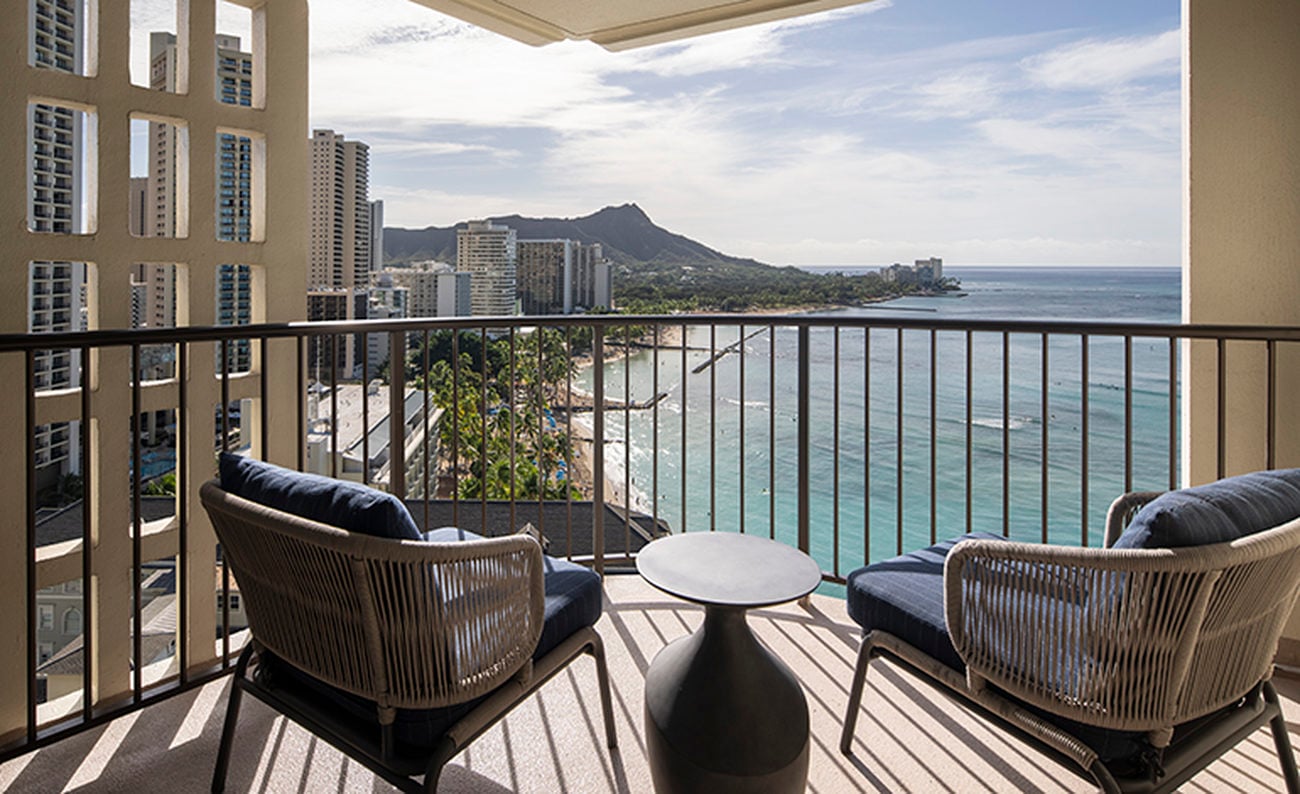 Two lounge chairs on a covered corner balcony facing the ocean and mountain