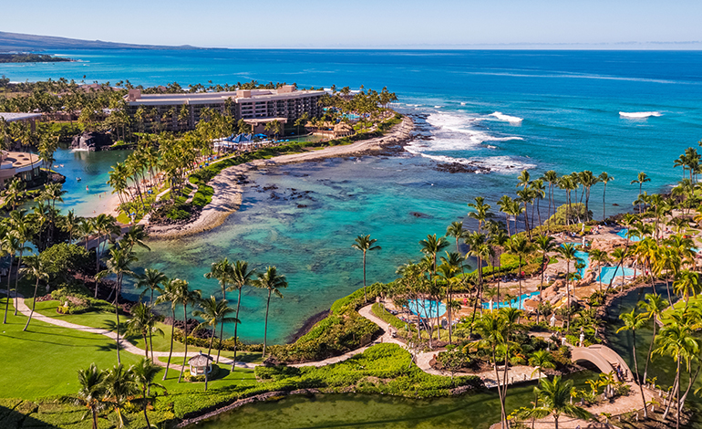 Aerial view of a turquois bay with pools, palm trees, and resort setting