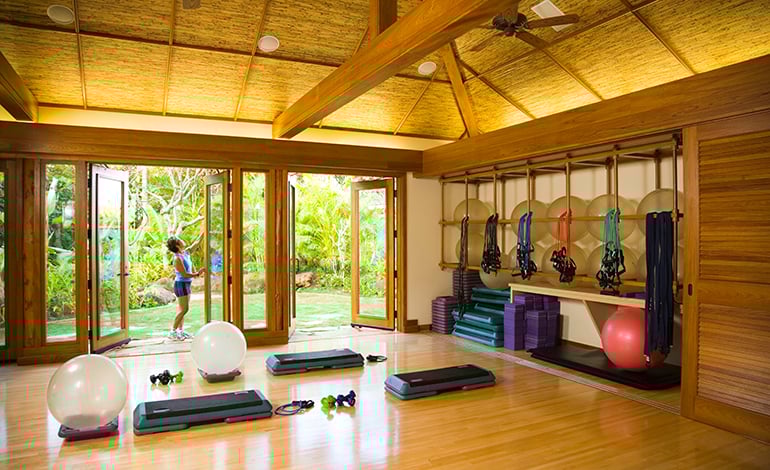 Cathedral ceilinged wood-toned yoga studio with steps, resistance band, and a woman opening the patio doors
