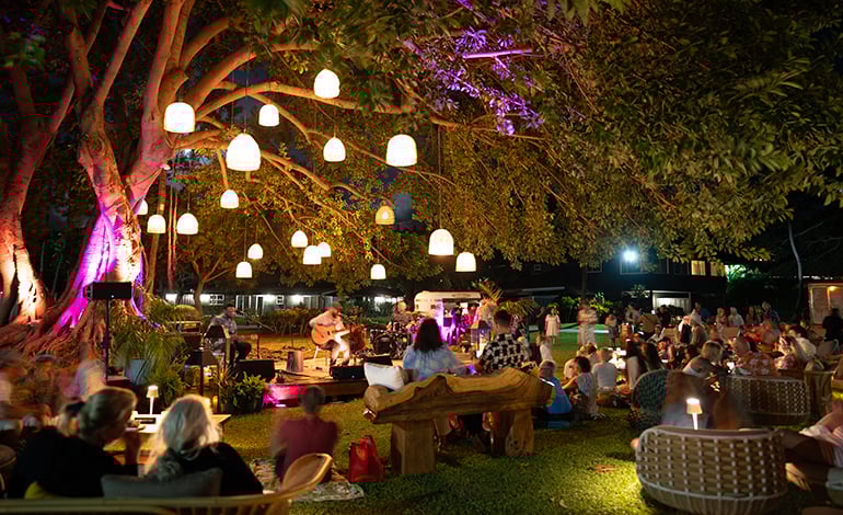 Evening performance in a garden with lit trees and seated guests