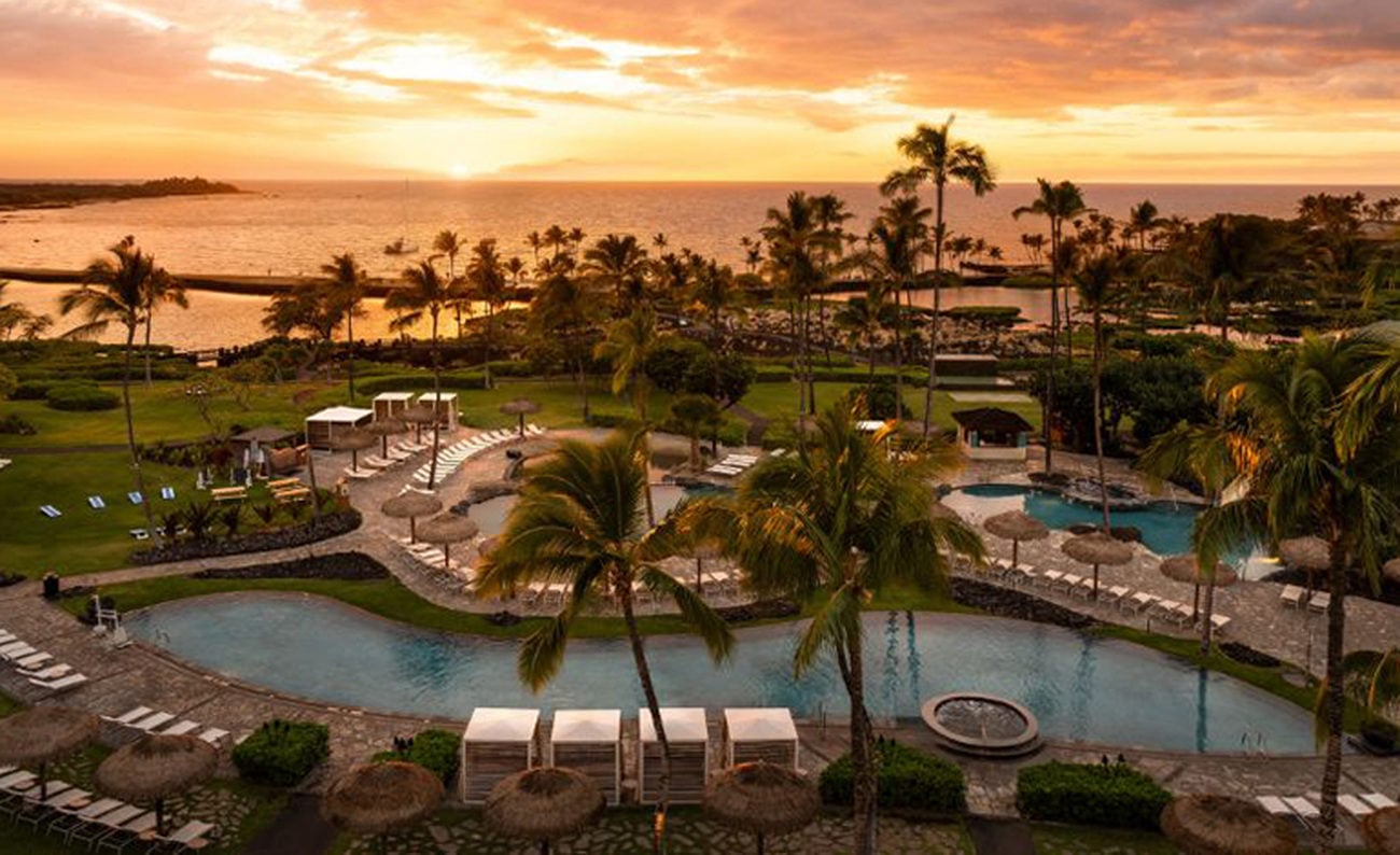Resort pool aerial view with an orange sunset over the water in the background