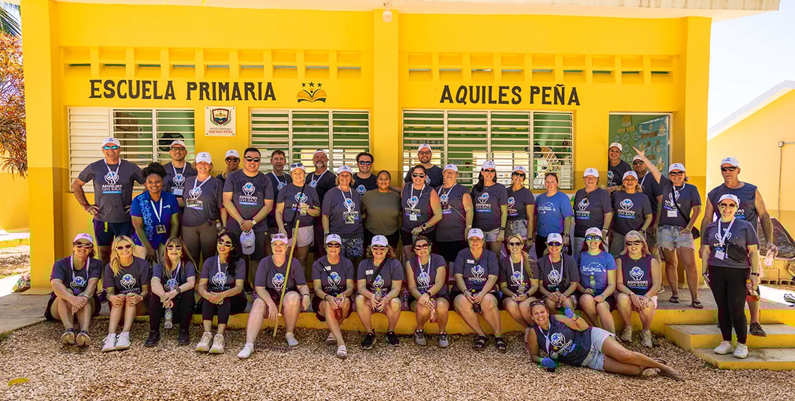 Group photos of volunteers in front of a freshly painted yellow school