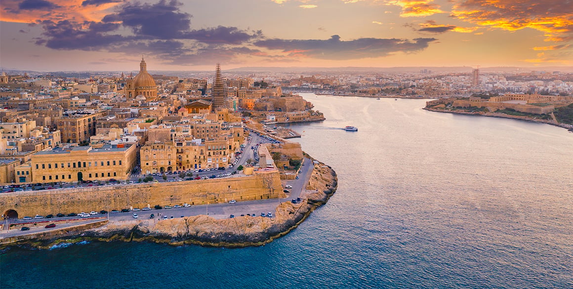 Sunset aerial view of Valletta's historic waterfront, harbor, and honey-colored buildings.