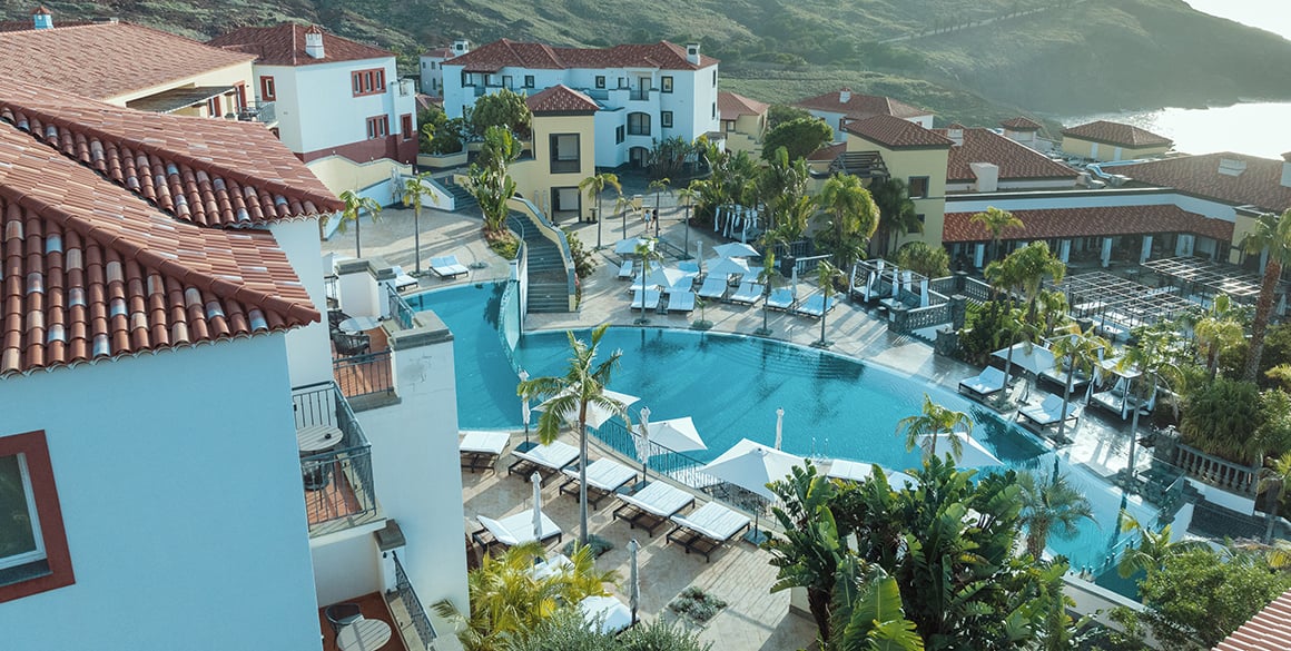 Overlook view of a resort pool and red tile-roofed buildings