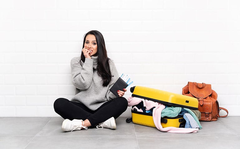 Young brunette woman looking nervous sitting on the floor next to a messy suitcase
