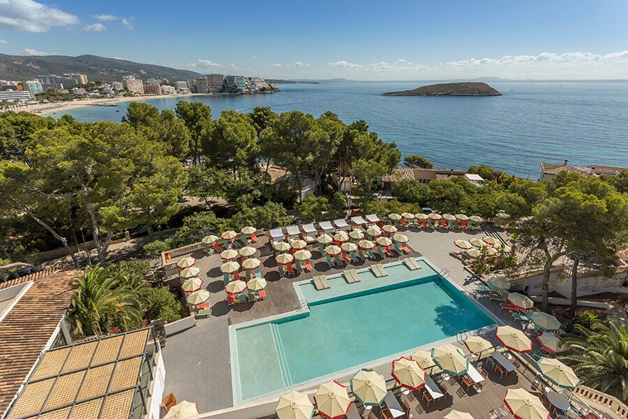 Aerial shot of rectangular pool with orange umbrellas around it and water with a distant island in the background