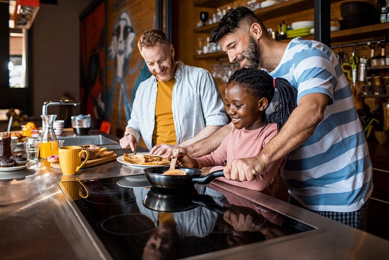 Two fathers and a daughter making crepes in a cafe