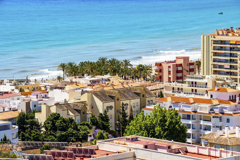 View of a bright blue sea and brightly colored resort-style city buildings in Torremolinos, Spain in the Costa del Sol