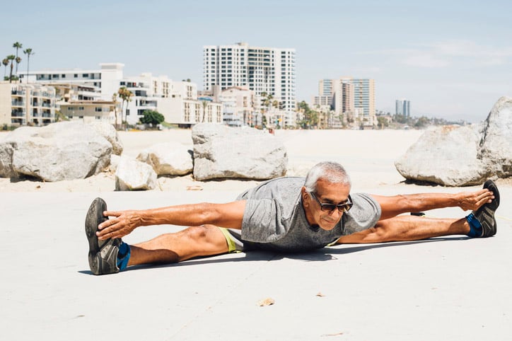 Senior man stretching in a split on a resort-filled beach