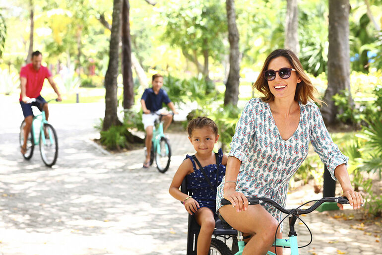 White woman riding a bike with a mixed-race child behind her, two males riding a bike behind her.