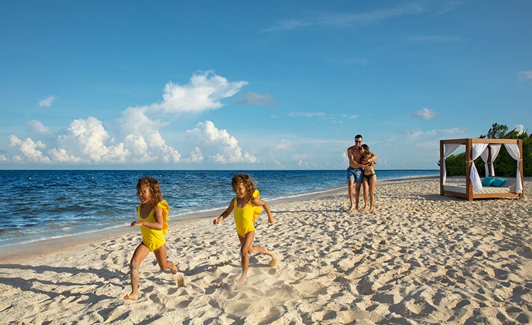 Two young girls running ahead of their parents on the beach at a Dreams Resort & Spa in Mexico