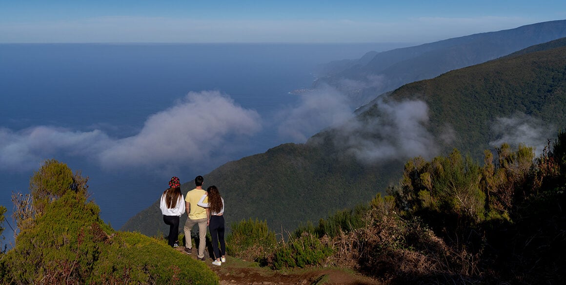 Two females and a man stand atop a cloudy summit