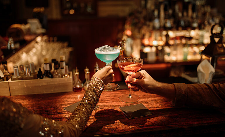 A woman and a man toast with cocktails at a bar