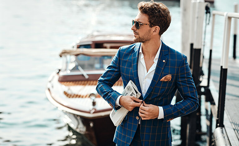 A fashionable man in a suit stands on the dock near a private boat