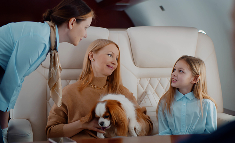 A flight attendant checks on a mother, daughter, and their pet Cavalier King Charles Spaniel in a first class cabin