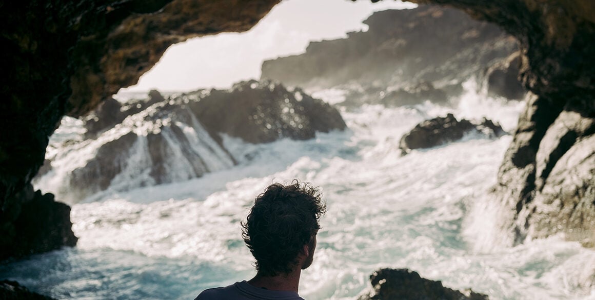Back of a man's head in a cave with crashing waves
