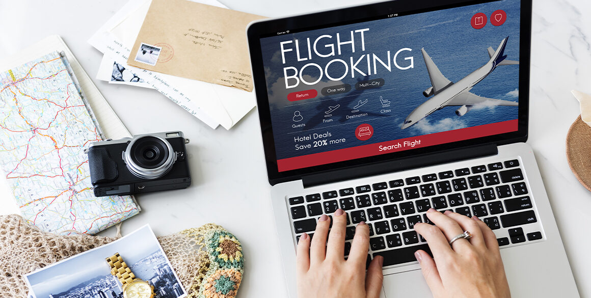 Stock image of laptop with Flight Booking written across the screen and travel-related props nearby