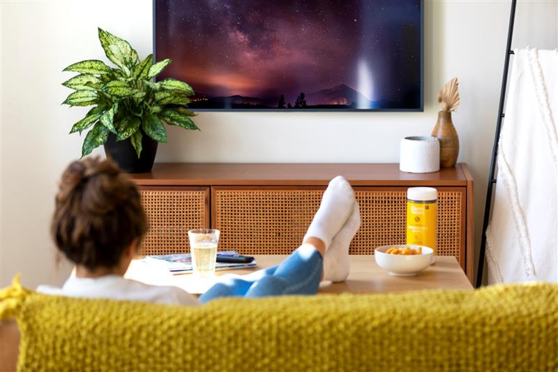 Woman sitting on a couch with her feet up watching tv, snack and sanitizing wipes on the table