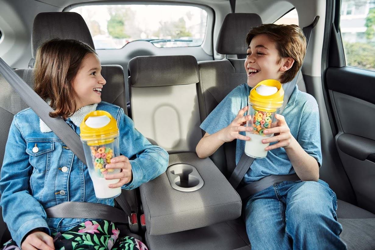 Boy and girl in the backseat of a car holding CrunchCups fulled with milk and cereal
