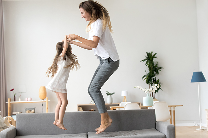 Mother and daughter holding hands and jumping on a couch