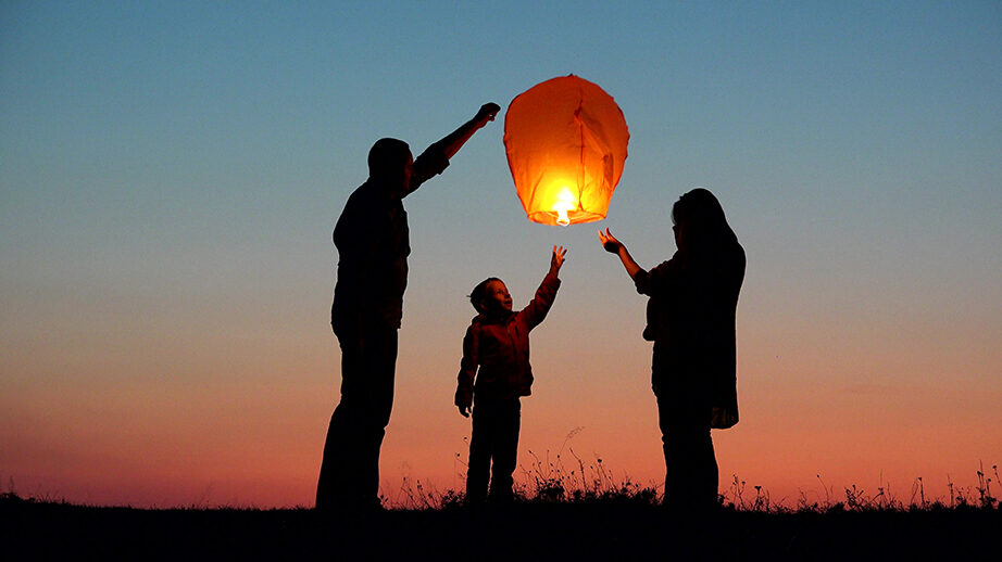 Two adults and a child pushing off a floating lantern