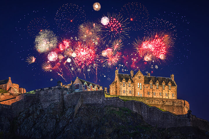 Building on a cliff at night with fireworks going off in the air behind it