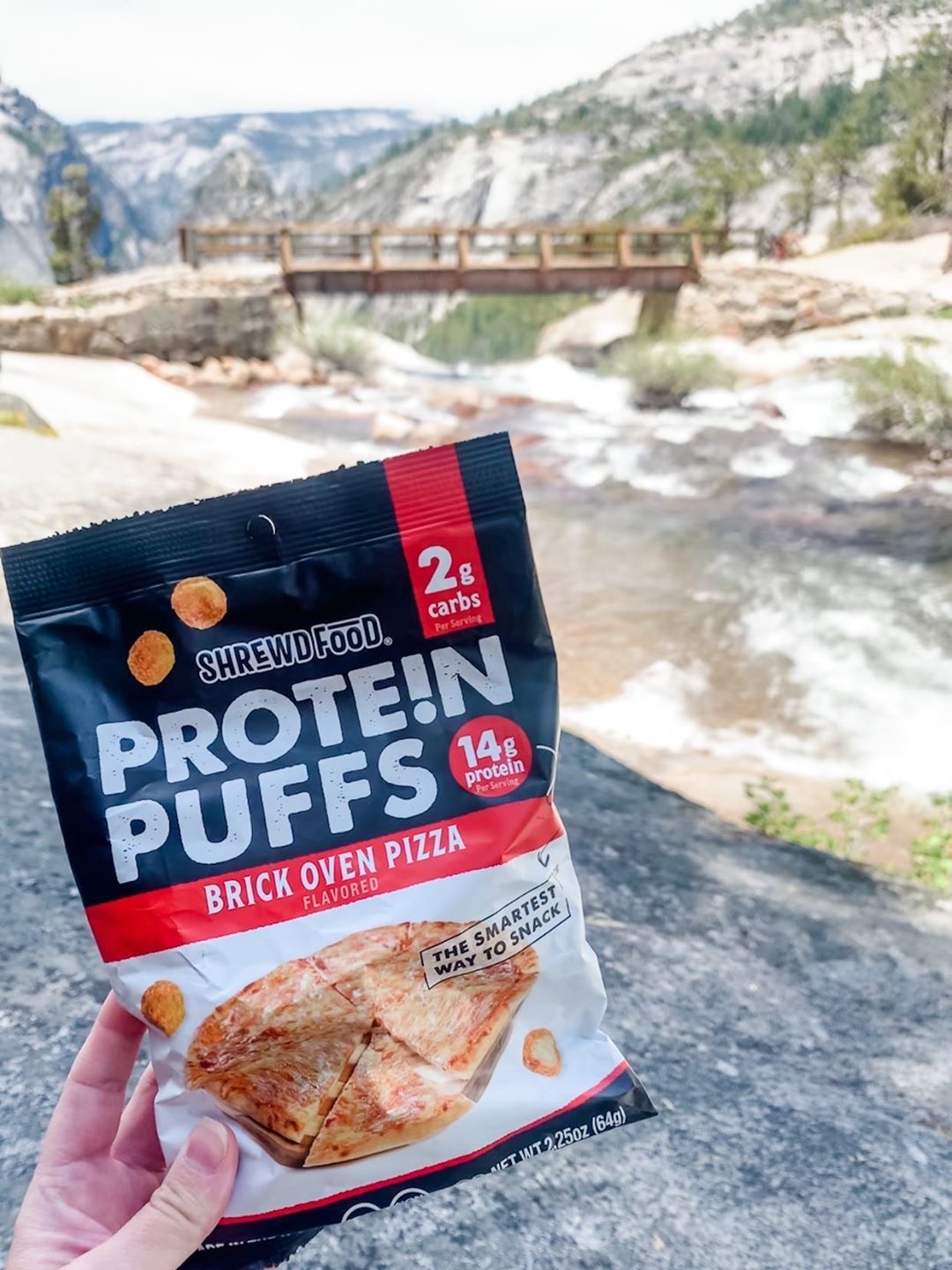 Package of shrewd food puffs in flavor brick oven pizza being held up by a river and mountains