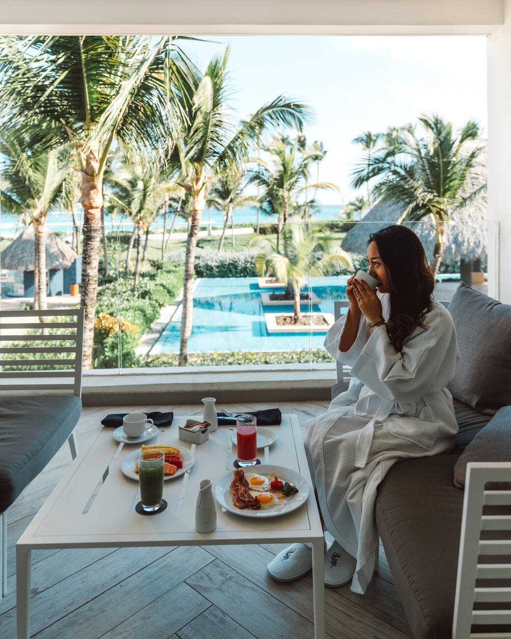 Woman in a bathrobe drinking coffee with breakfast on the table overlooking the ocean