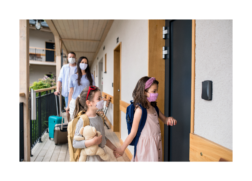 Family with masks on bringing luggage into their hotel room