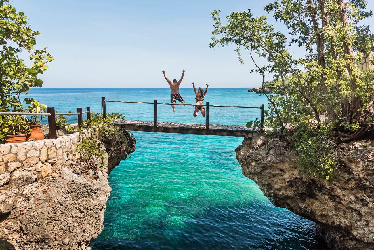 A man and a woman jumping off of a low wooden bridge into the ocean below.