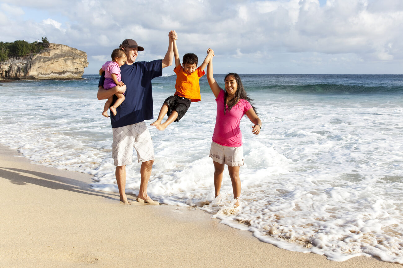 A family walks along the shoreline, lifting their son into the air above the waves.