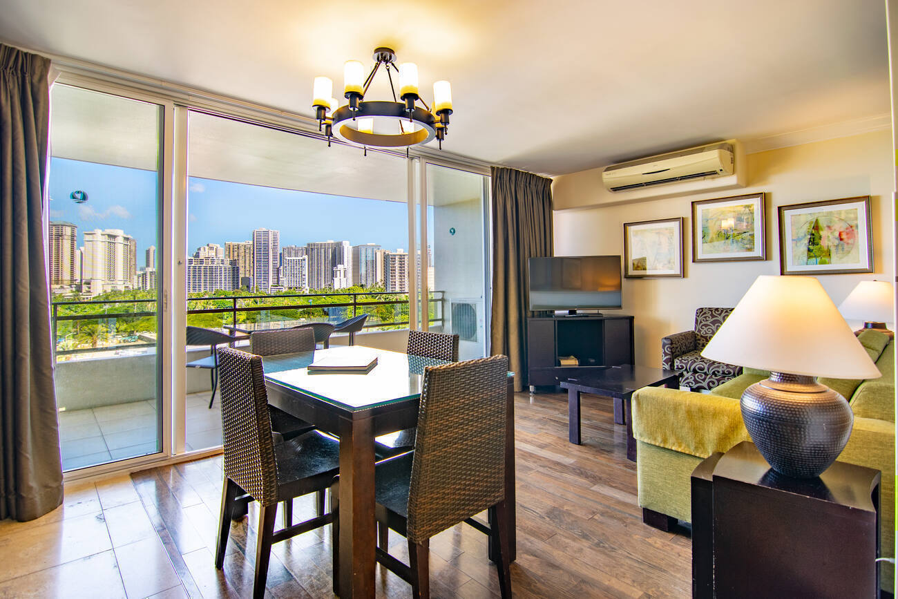 An open dining and sitting area in a Two Bed Partial Ocean View unit with the Honolulu skyline visible through floor-to-ceiling glass doors.