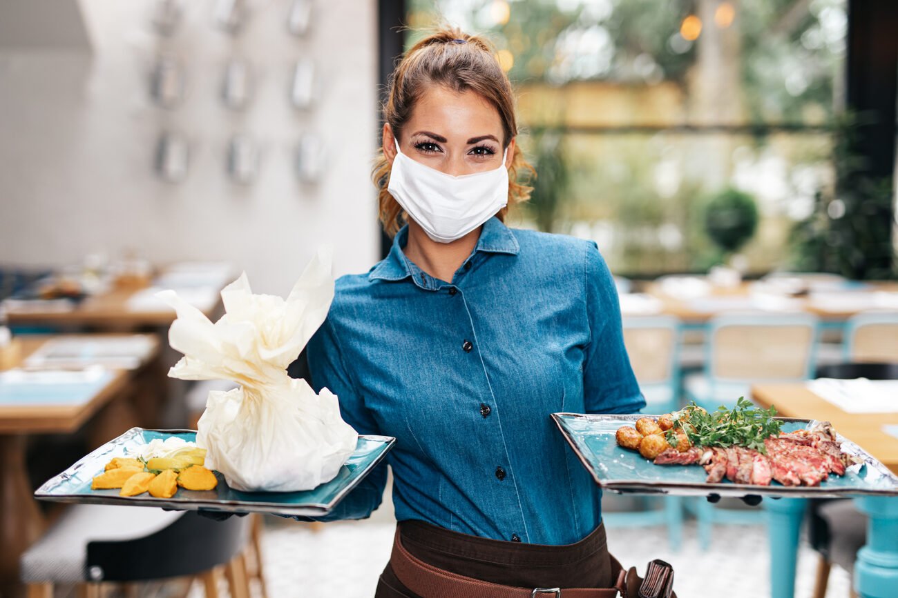 Waitress with a mask on serving two dishes