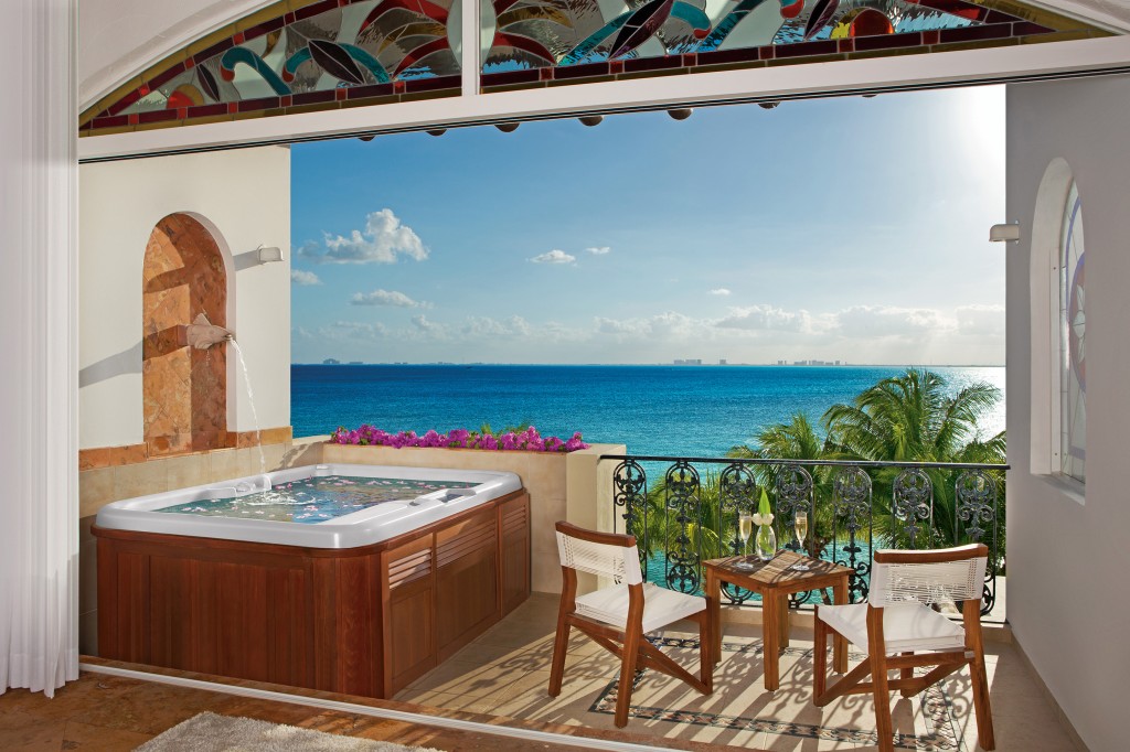 A Jacuzzi, table, and chairs on a terrace overlooking the ocean.