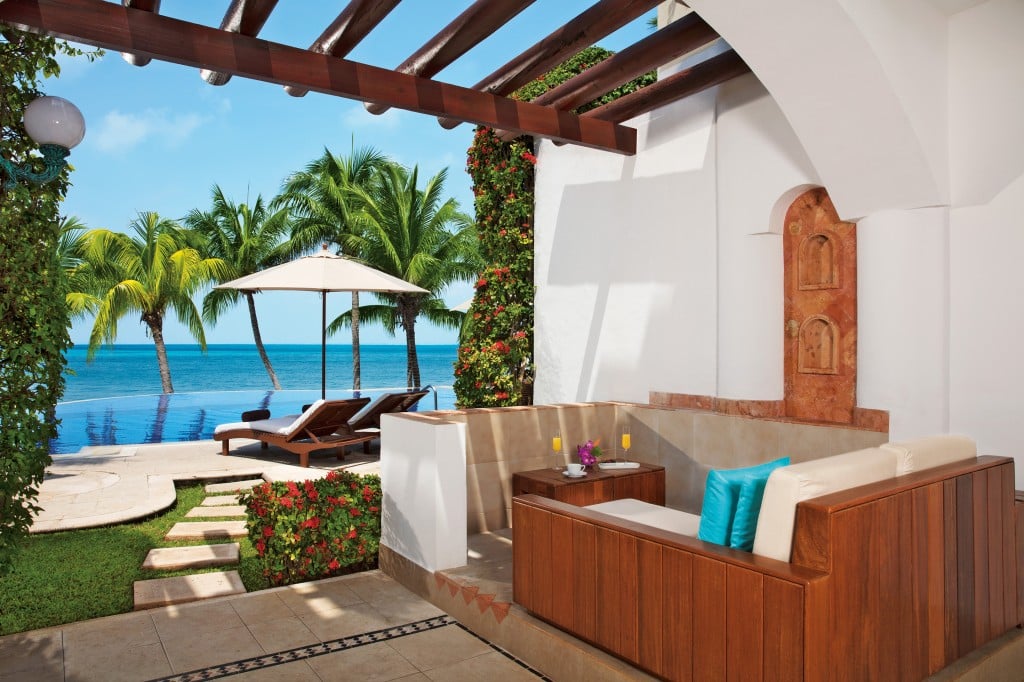 The seating area of a terrace with a pathway leading to a private infinity pool beside the ocean.