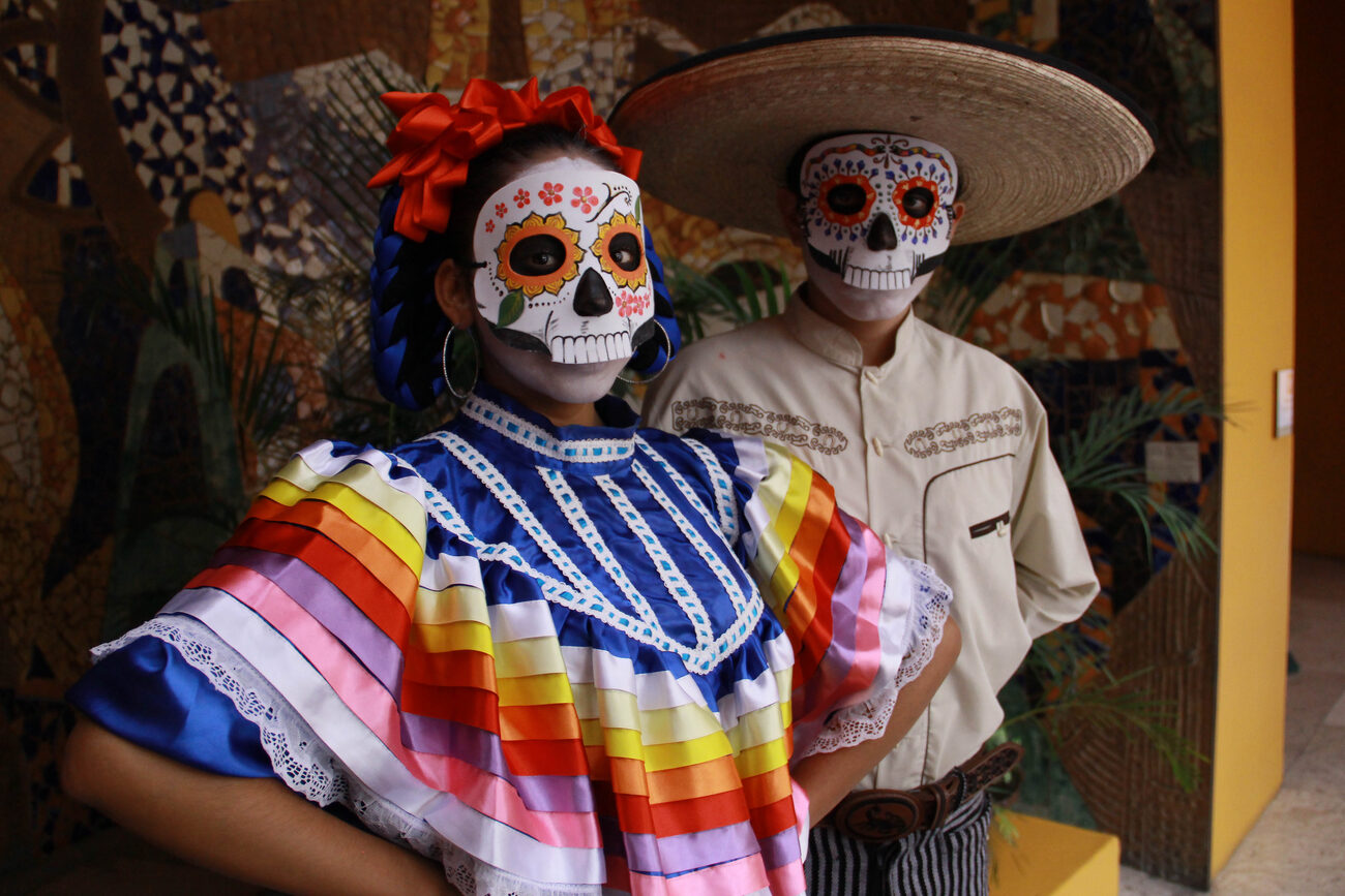 A man and woman wear traditional shirts and skull masks for the Day of the Dead