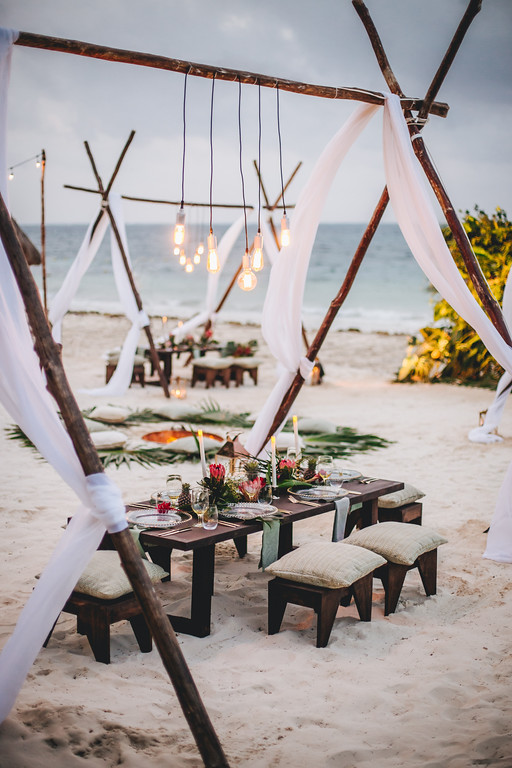 Dining tables set up on the beach with lights