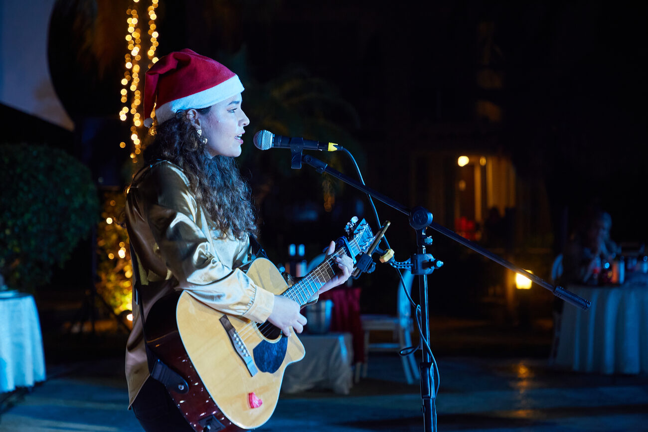 Woman in a Santa hat playing guitar and singing on stage