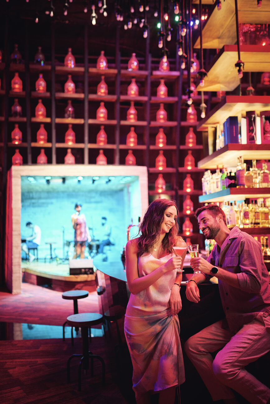 People drinking at a bar with a performer in the back