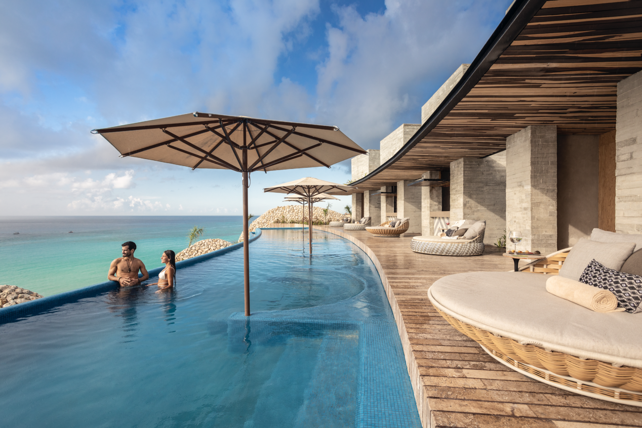 Round lounge chairs by an infinity pool people are swimming in