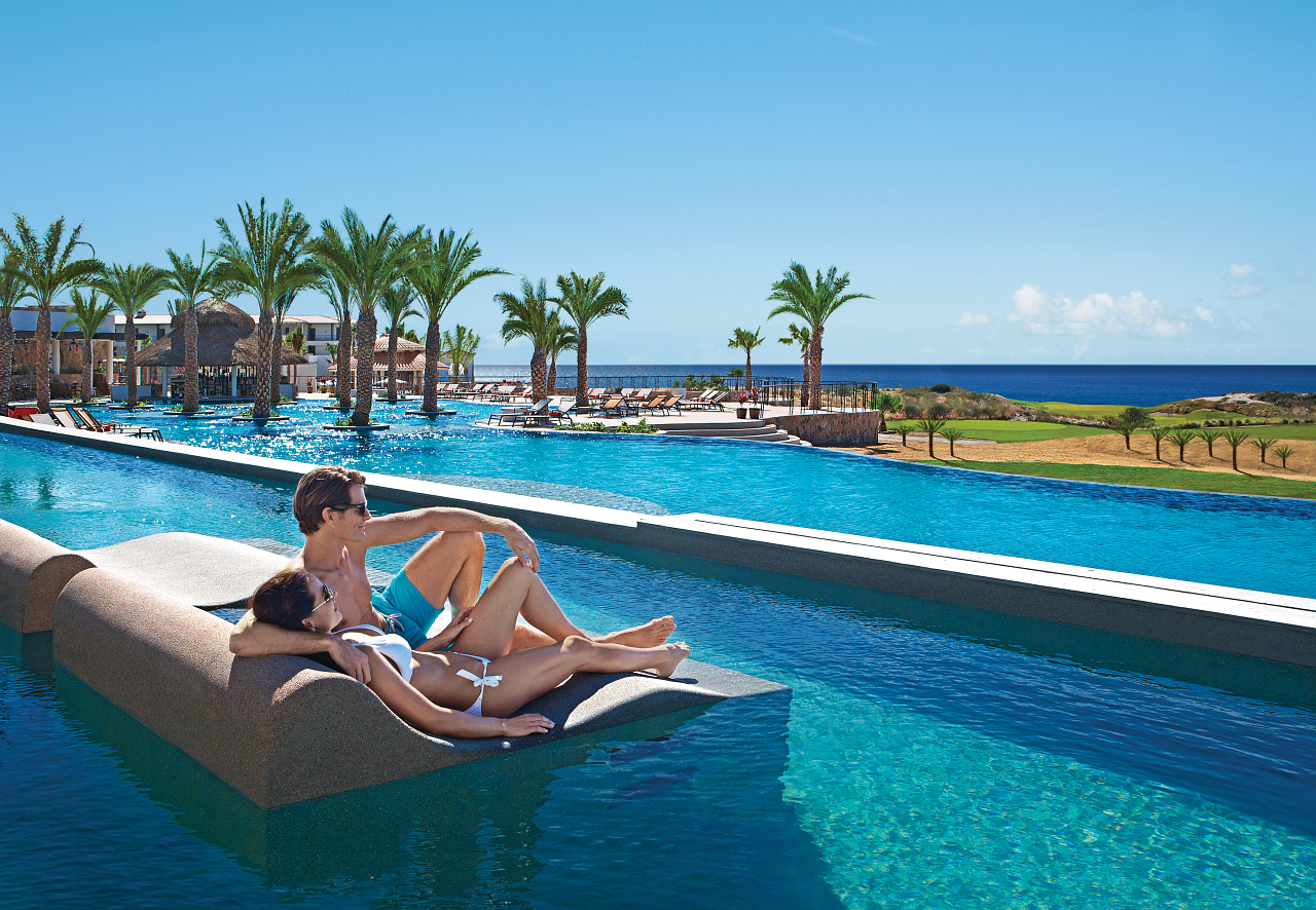 Man and woman on a pool lounger overlooking the ocean.