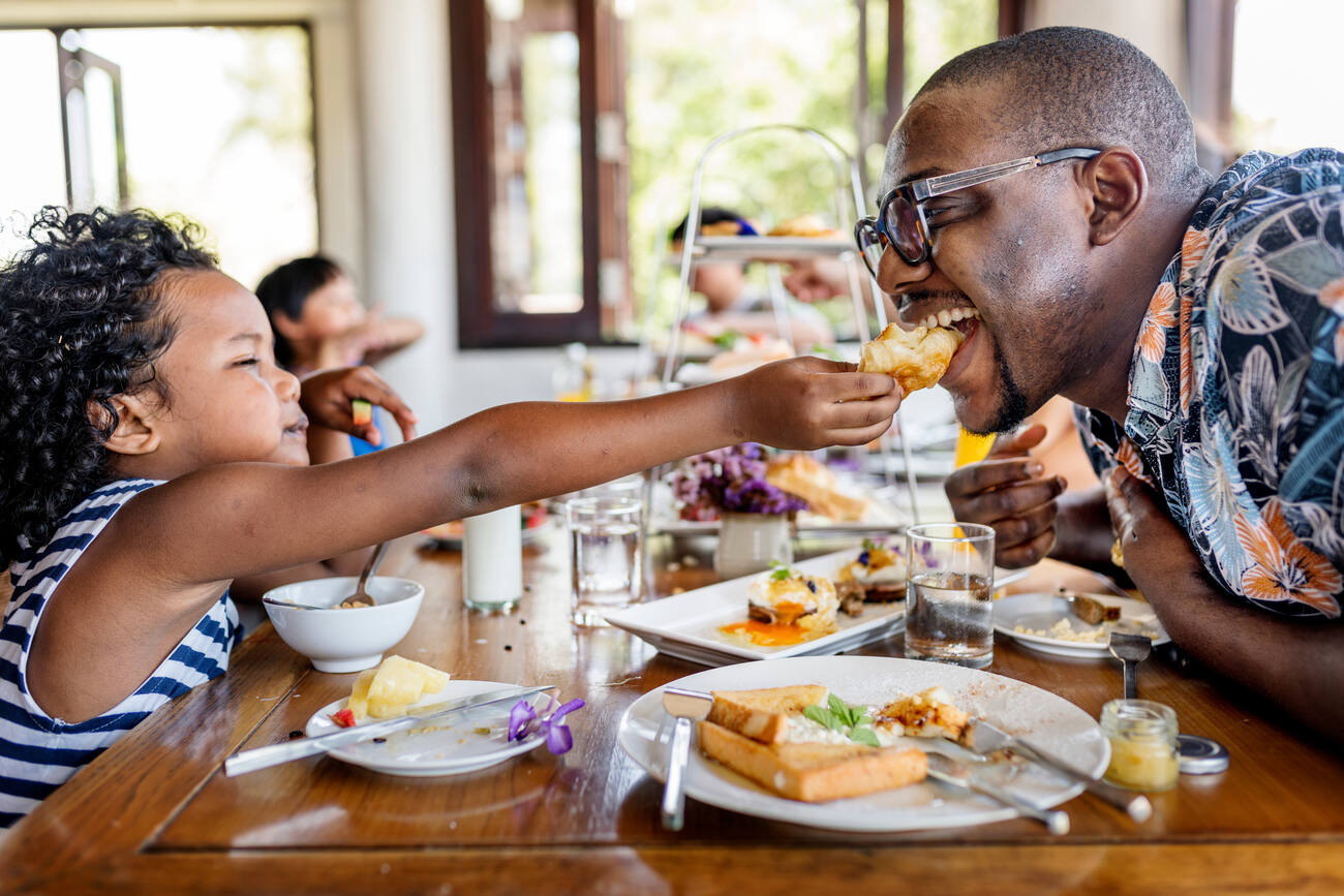 Child feeding food to a man at a dinner table