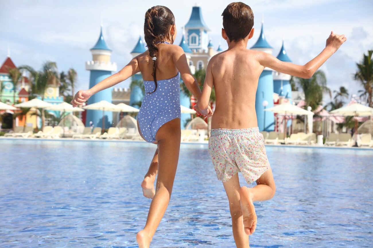 Two kids holding hands running into a pool