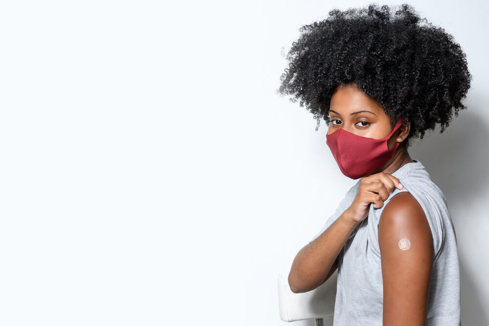 Woman wearing a mask and showing her arm with a bandage from a shot 