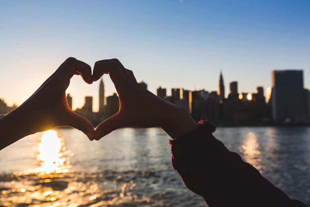 Hands making a heart at the water and city line