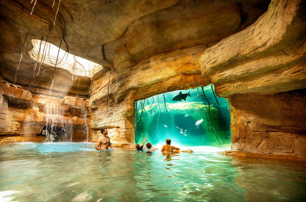 People swimming in a cave looking at fish through a glass wall