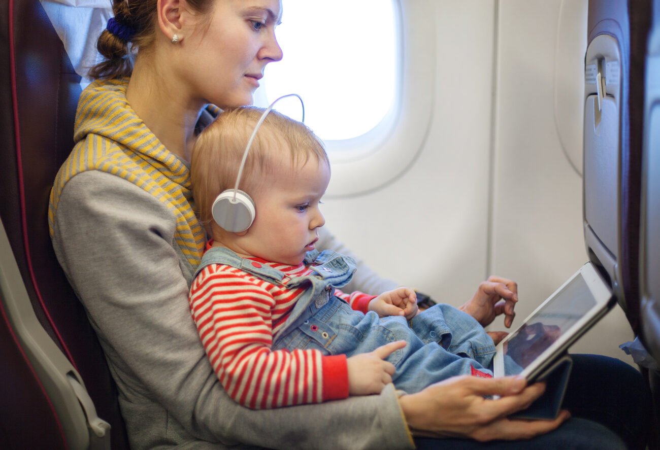 Woman holding her child on a plane playing on an iPad