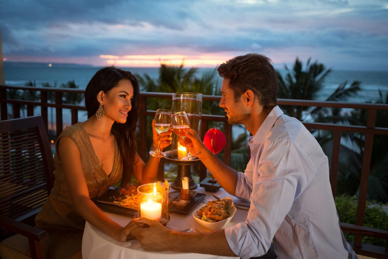 Couple eating at a candlelit dinner table overlooking the ocean
