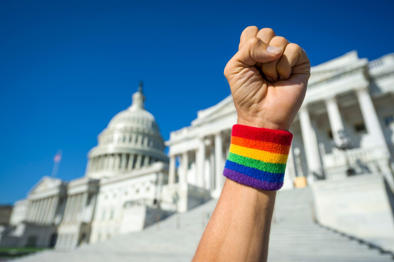 Hand making a fist with a pride sweat band in front of the capital